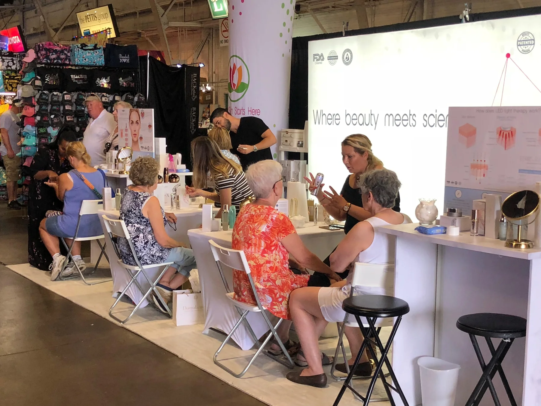 Visitors seated at Mazel demonstration counters in a busy exhibition hall